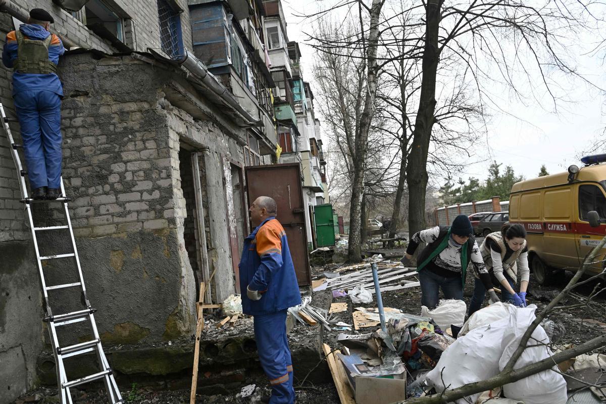 Los trabajadores del servicio de gas revisan una tubería de gas mientras los residentes locales limpian los escombros en un edificio residencial dañado después de un ataque militar en la ciudad de Kostyantynivka.