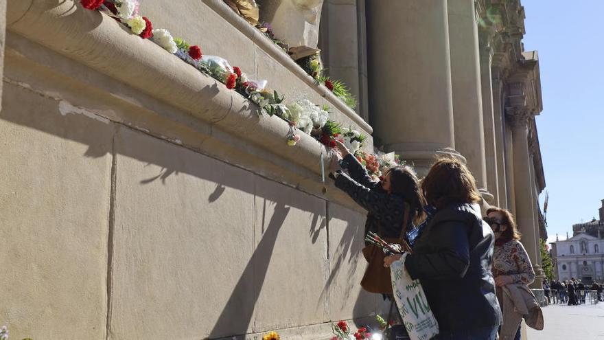 Varias personas depositan flores en el exterior de la Basílica del Pilar