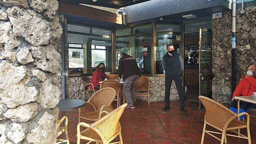 Manuel González, a la puerta de su negocio, con varios clientes en la terraza. 