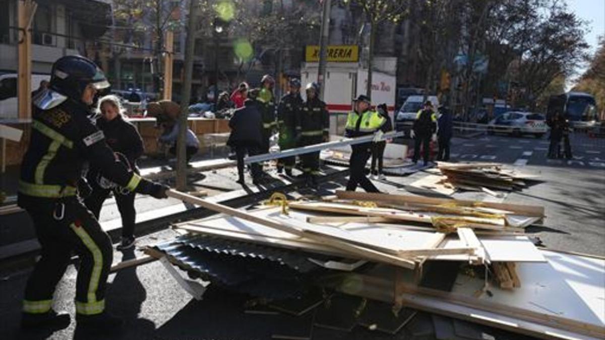 Bomberos y guardias urbanos retiran piezas de uno de los puestos derribados por el viento en la Fira de Reis de la Gran Via de Barcelona, ayer.