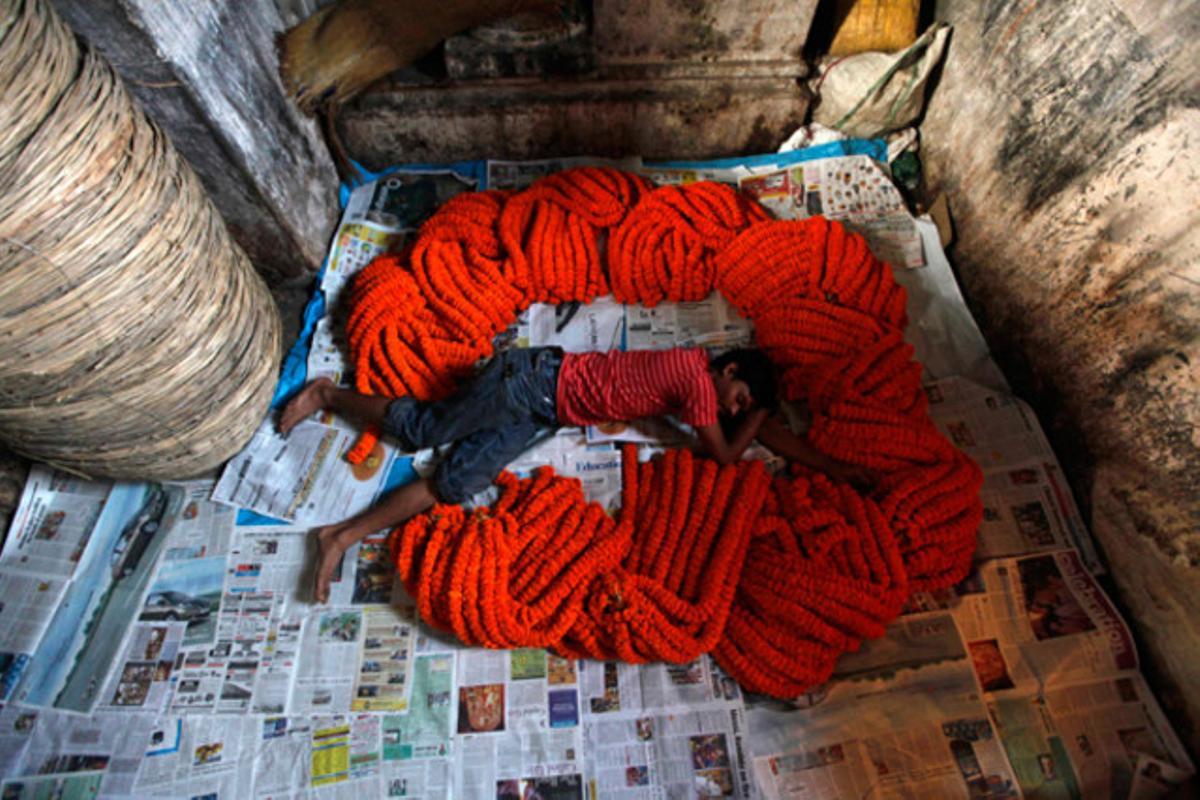 Un treballador dorm entre garlandes de flors dies abans del festival religiós més important per a creients hindús, el Durga Puja, a Calcuta, Índia. En l’hinduisme, la deessa Durga representa el poder i el triomf del bé sobre el mal.