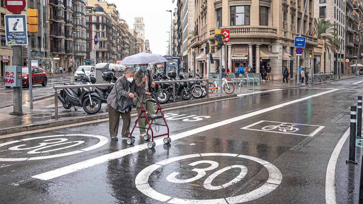 Dos personas mayores cruzan por donde no deberían en el origen de la calle de Pelai, con la velocidad limitada a 30