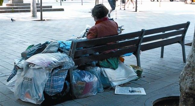 Una mujer sintecho con sus cosas en un banco de la calle de Còrsega.