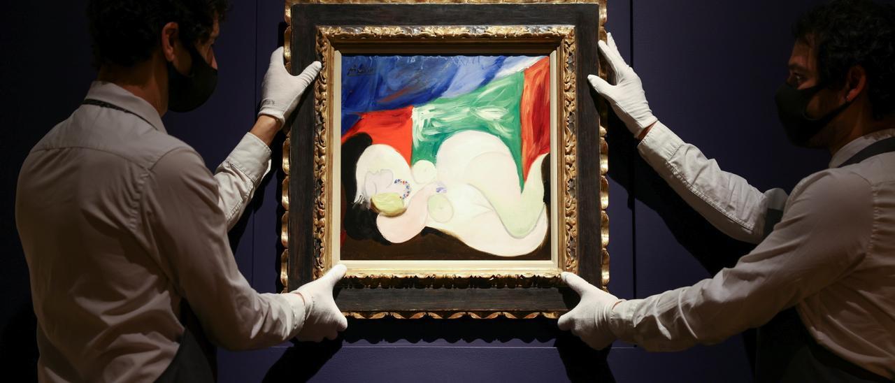 Gallery assistants hold artwork titled &#039;Femme nue couchee au collier&#039; by painter Pablo Picasso during a photocall at Christie&#039;s auction house, in London