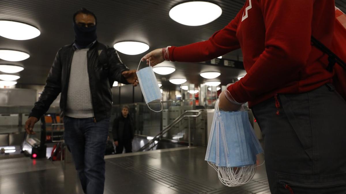 Un miembro de Creu Roja reparte mascarillas en el  metro de Barcelona.