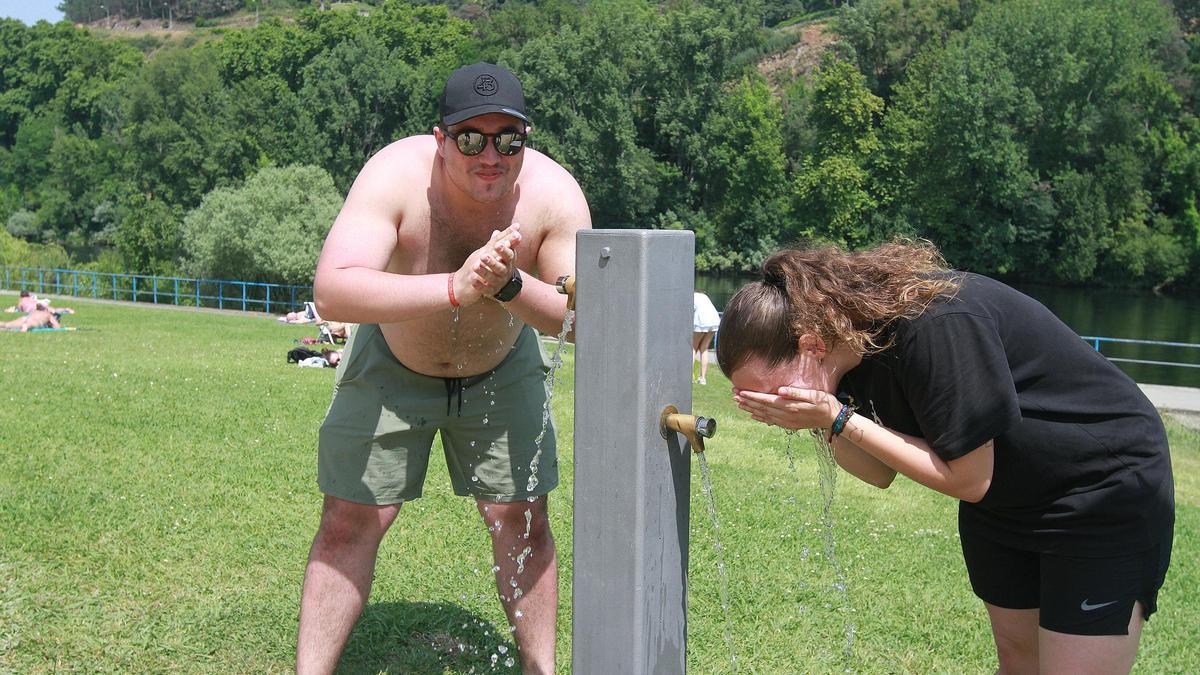 Dos personas se refrescan en una fuente del parque de Oira.