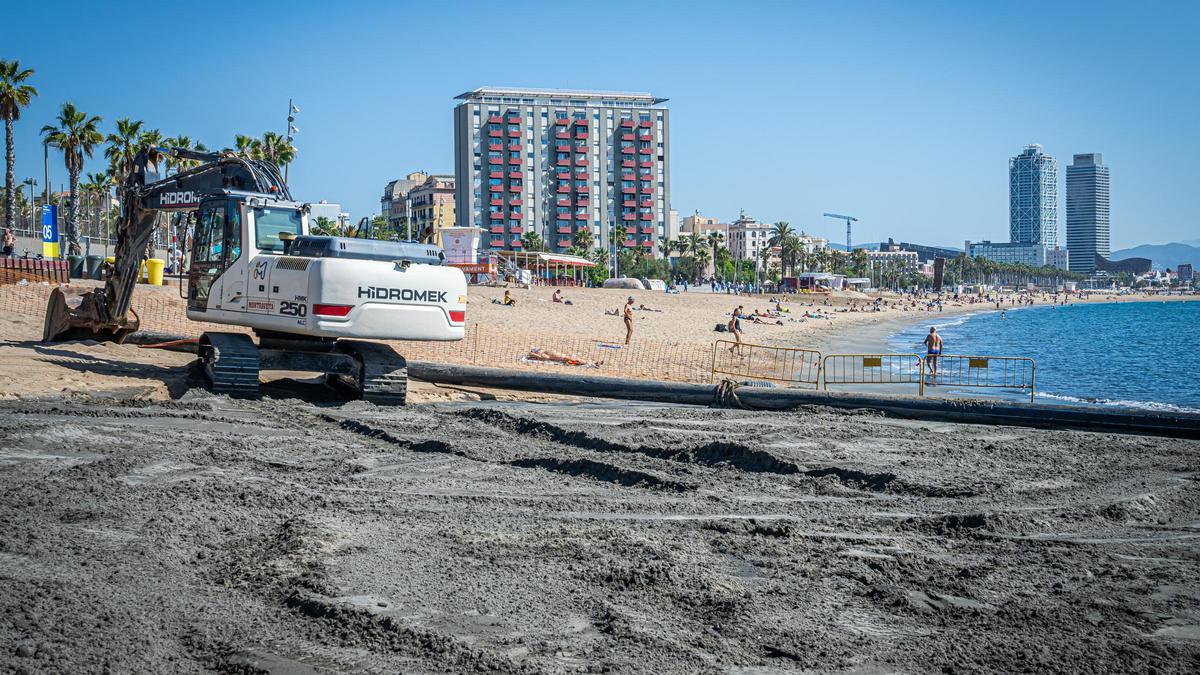 Una grúa y una tubería para arrojar arena desde un barco draga en la playa de Sant Sebastià, en Barcelona.