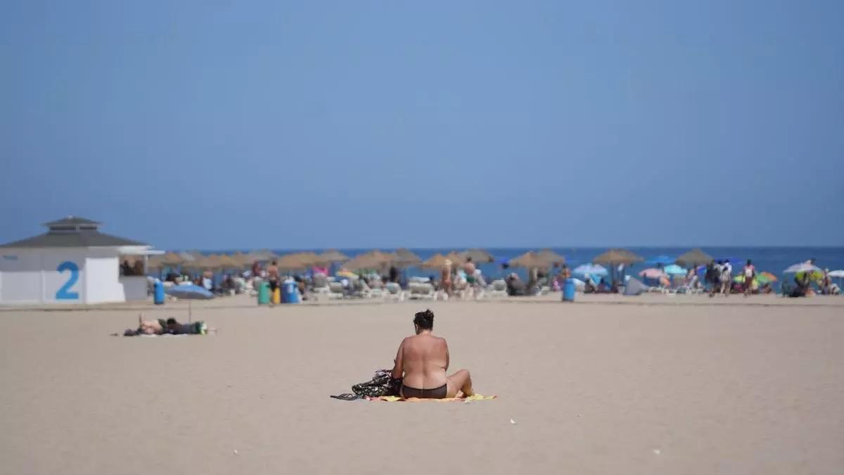 Una persona asseguda sobre una tovallola a la platja durant la quarta onada de calor de l’estiu, el 22 d’agost de 2023, a València, País Valencià (Espanya)