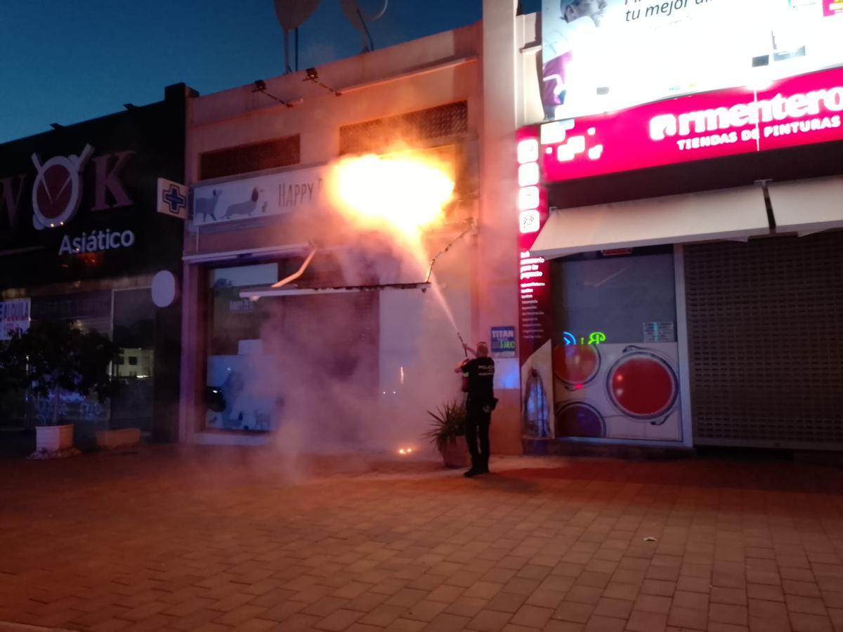 Un agente sofoca las llamas en la fachada del negocio.