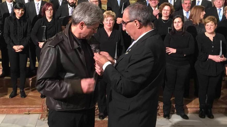 El presidente de la Coral Polifónica, Tino Sierra, coloca la &quot;Avellana de plata&quot; en la solapa a José María Aladro, ayer en la iglesia parroquial de Infiesto.