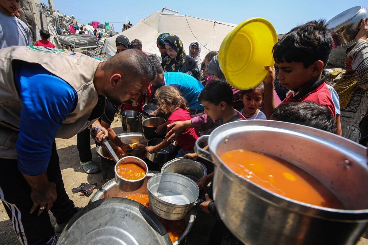 Palestinos desplazados, entre ellos mujeres y niños, esperan recibir alimentos distribuidos por organizaciones humanitarias en Gaza.