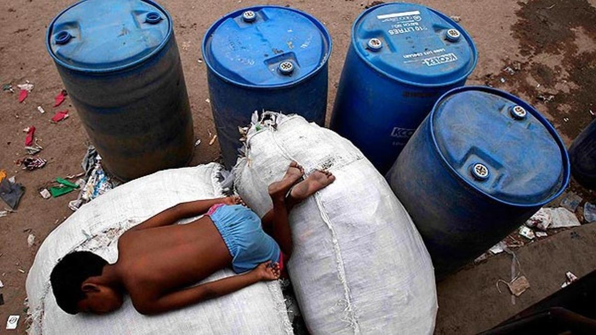 Un nen dorm envoltat de contenidors d’aigua buits en una zona industrial de Nova Delhi (Índia).