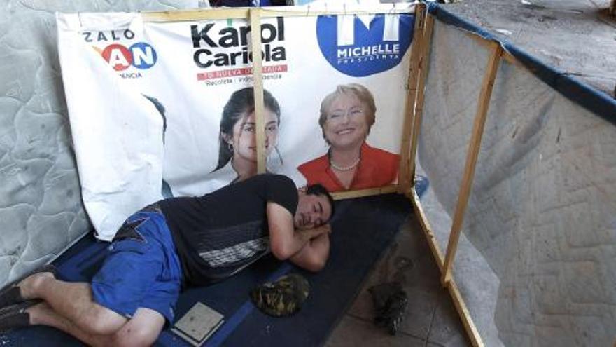 Un hombre duerme junto a un cartel de la candidata Michelle Bachelet.