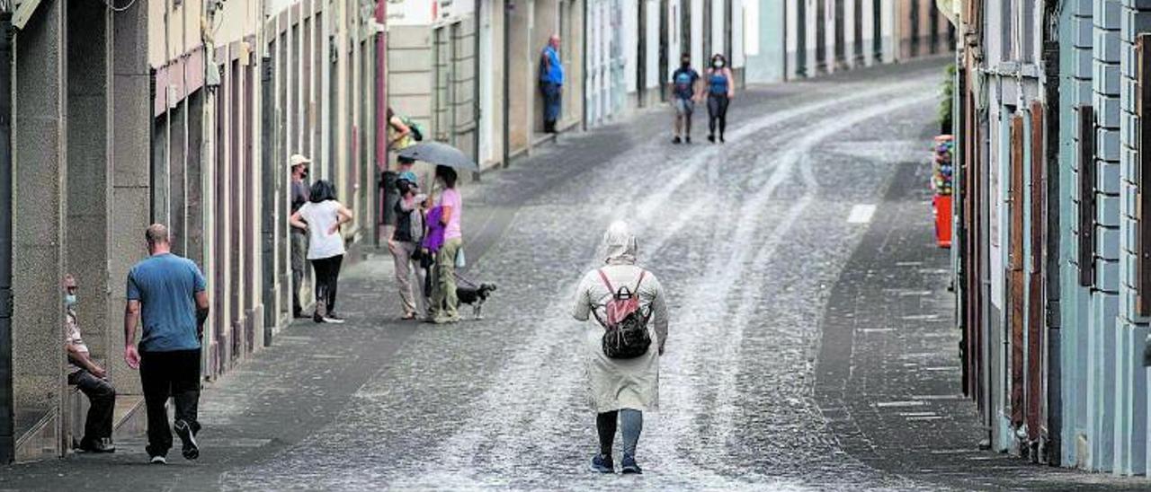 Las calles de Santa Cruz de La Palma, cubiertas por un manto de ceniza mientras los palmeros se protegen con paraguas y chubasqueros.