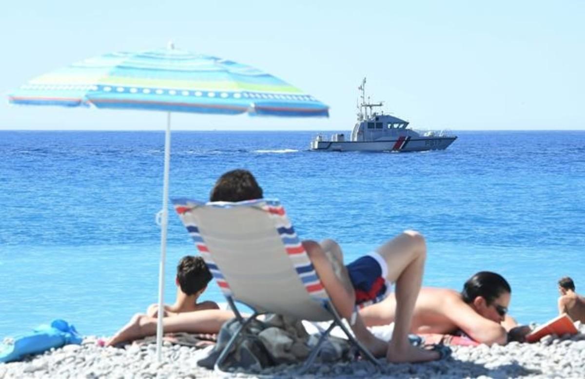 Ciudadanos disfrutan de la playa en Niza, mientras una lancha de la Gendarmeria patrulla en el mar