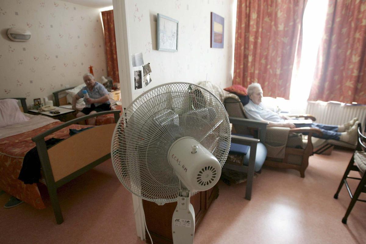 Unas personas mayores se protegen del calor con un ventilador. 