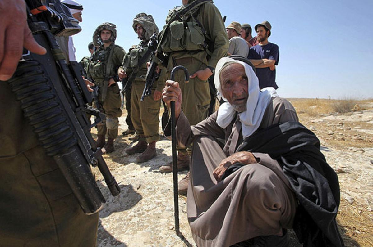 Un palestí assegut a terra es nega a abandonar el lloc mentre l’envolten soldats i colons israelians, a Sussa, a prop de Cisjordània.