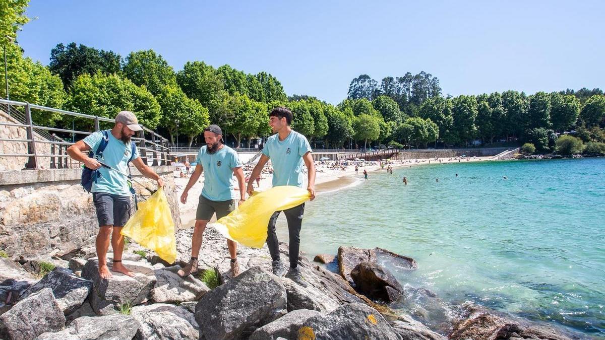 Tres de los participantes en el proyecto "Mil Playas" durante los trabajos de limpieza en una playa.