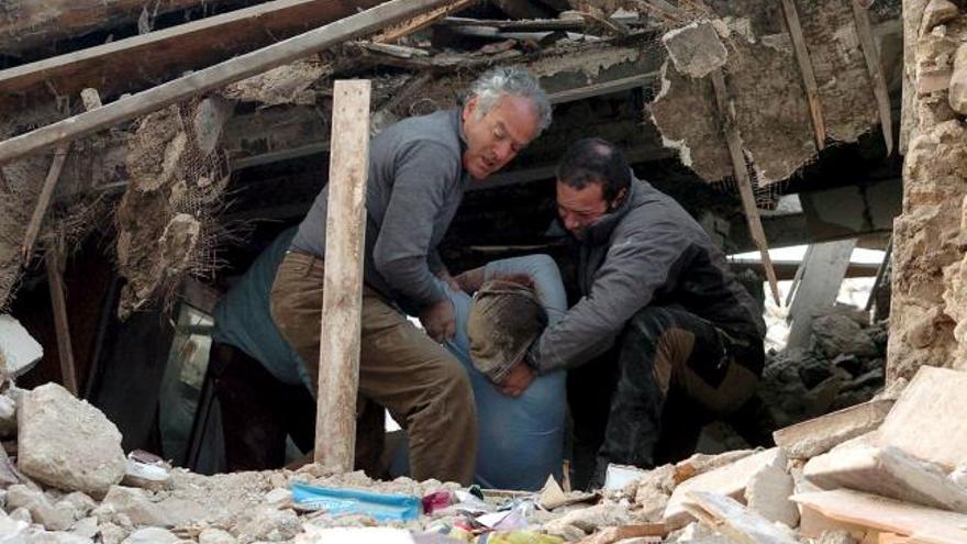 Dos hombres sacan un cadáver de entre los escombros