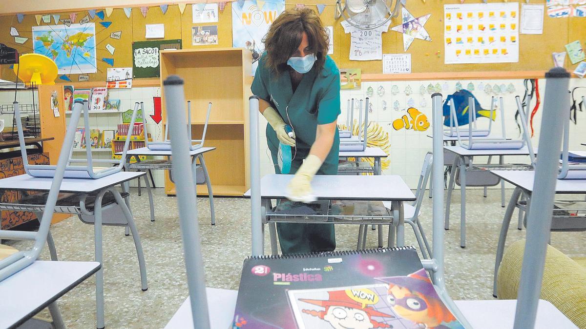 Una mujer limpia las mesas y sillas de un colegio.