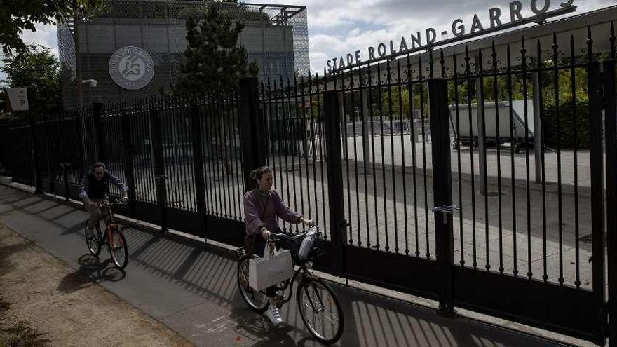 Dos parisinos pasan por delante de la puerta de las instalaciones de Roland Garros. // Ian Langsdon