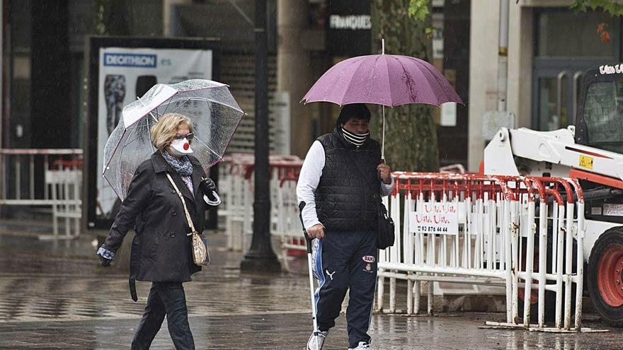 Dues persones caminen sota la pluja amb les mascaretes posades
