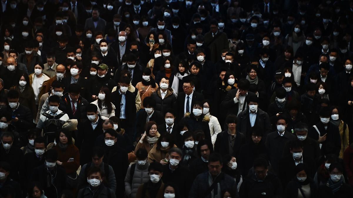 Los viajeros vestidos con máscaras se dirigen al trabajo durante la hora pico de la mañana en la estación de tren de Shinagawa en Tokio el 28 de febrero de 2020. El índice Nikkei clave de Tokio se desplomó casi un tres por ciento en la apertura del 28 de febrero después de las liquidaciones de inversores estadounidenses y europeos preocupados por el impacto económico del brote de coronavirus