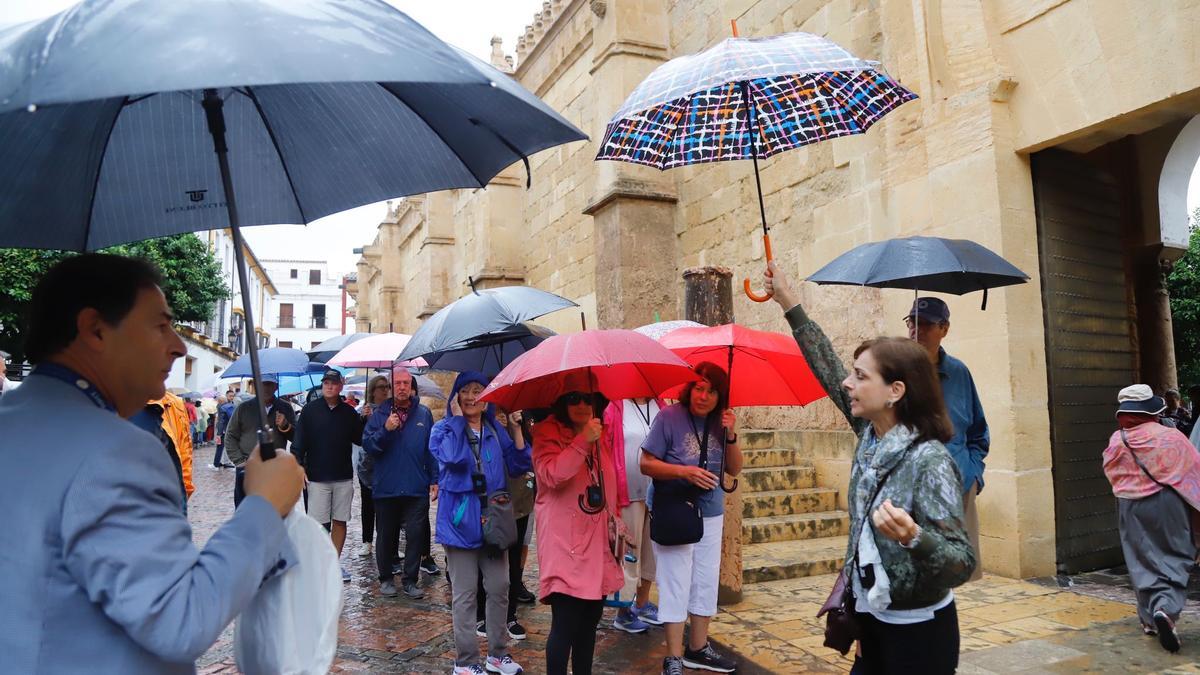 Un grupo de turistas en el entorno de la Mezquita-Catedral, se protege de la lluvia con paraguas, este viernes en Córdoba.