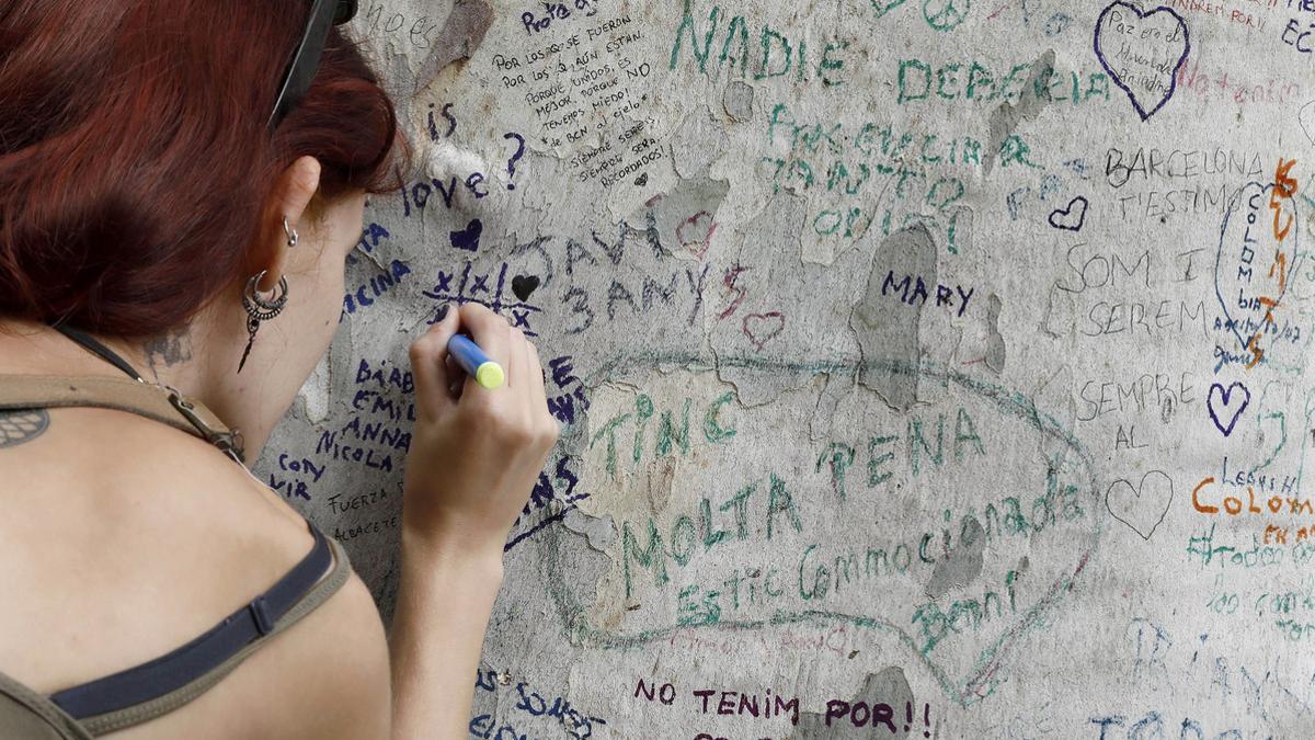 Una joven muestra sus condolencias con un mensaje escrito en un árbol de la Rambla de Barcelona.