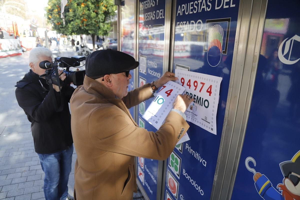 El delegado de la Sociedad Estatal de Loterías y Apuestas del Estado en Córdoba coloca un cartel con el primer premio del niño en el quiosco de Gran Capitán donde se ha vendido parte.