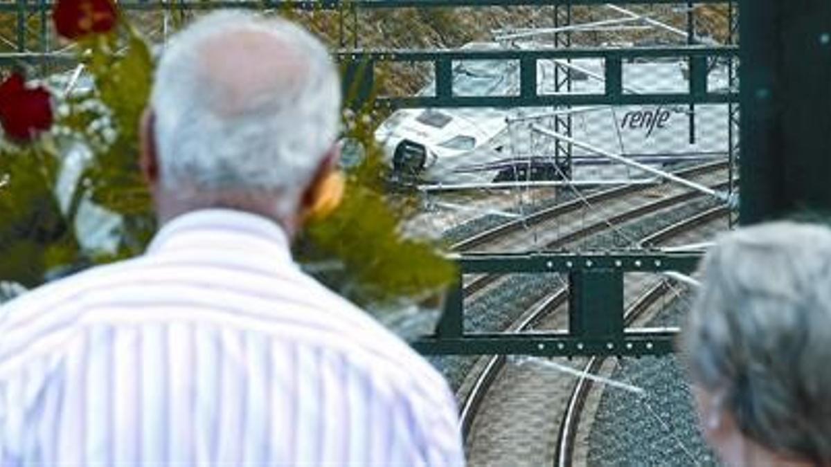 Destrozado  8Dos vecinos de la zona observan, junto a flores dejadas por ciudadanos, la curva del accidente, en la que todavía está una de las máquinas accidentadas.