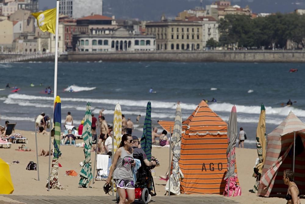 Gijoneses y visitantes se lanzan a la playa en una jornada calurosa.