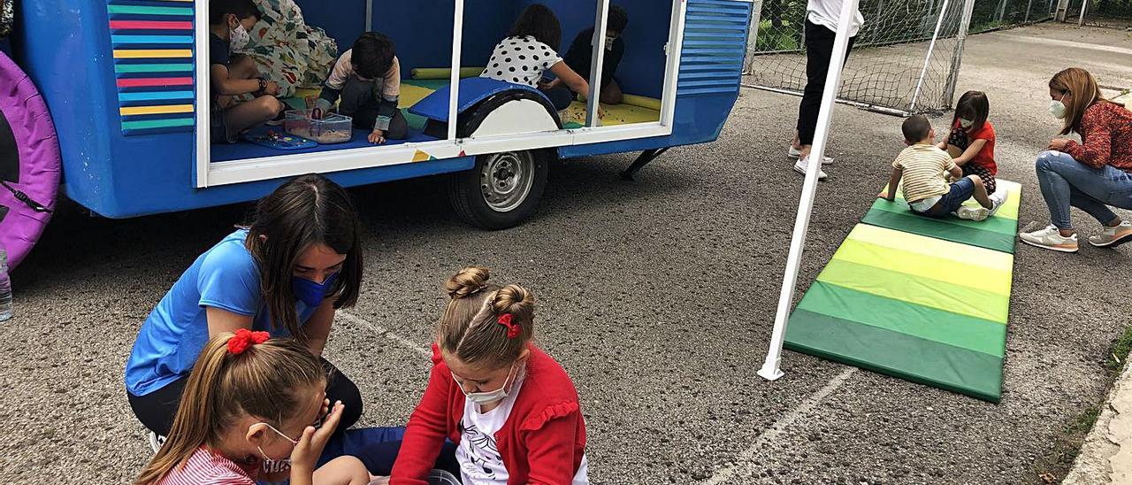 Arriba, la caravana, con varios niños participando en las actividades. Debajo, a la izquierda, uno de los trabajos que se hacen con los niños. A la derecha, Laura García y Eva Rodríguez.