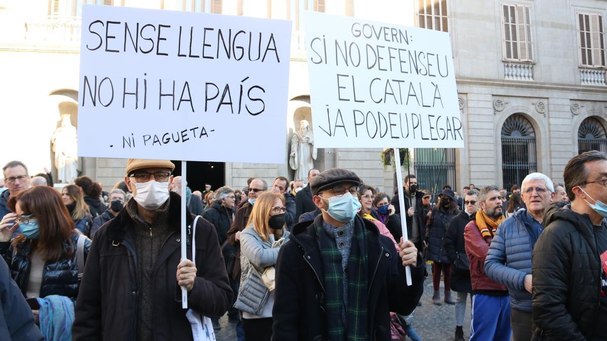 Dos manifestants mostren cartells defensant la immersió lingüística en català a l'escola durant una protesta a la plaça de Sant Jaume de Barcelona