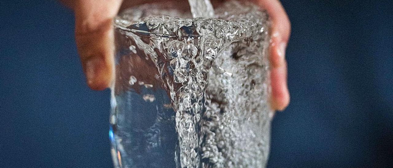 Una mano sujeta un vaso lleno con el agua que sale de un grifo.