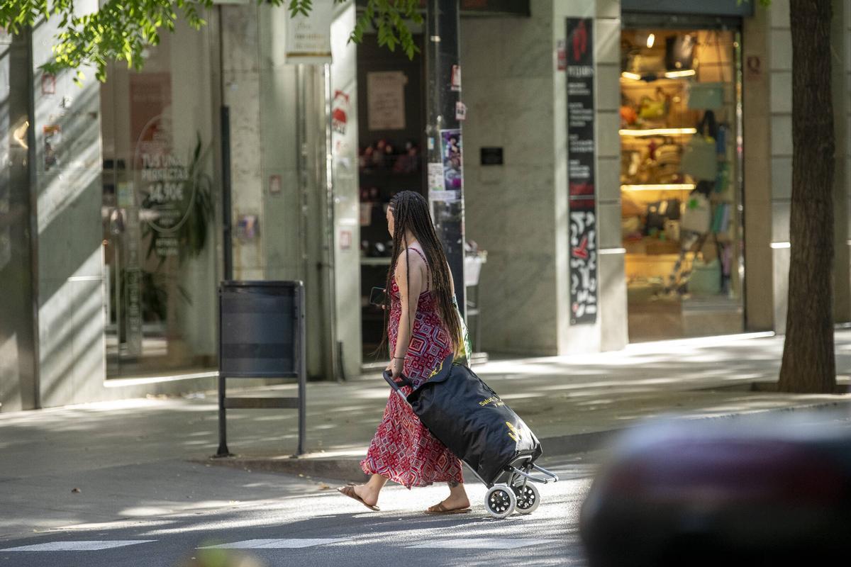 Una mujer criza la calle con un carrito de la compra. Sants-Creu Coberta, eje comercial más largo de España. Barcelona, 18 de junio de 2026. Foto: Belén González / EP