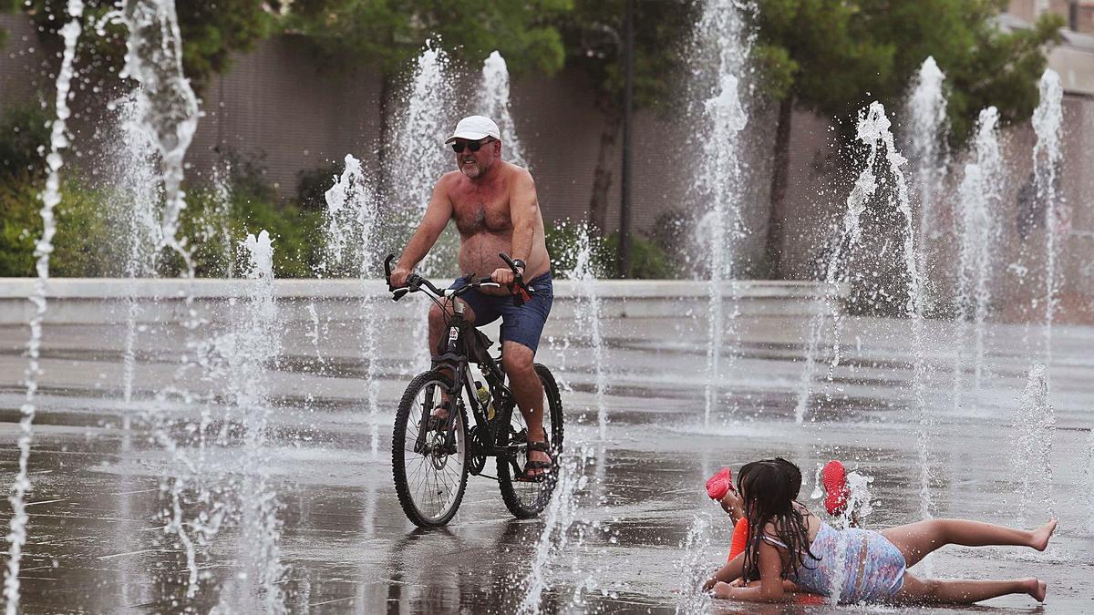 Un ciclista y unos niños se refrescan de las altas temperaturas en el Par Central de València. | J.M. LÓPEZ