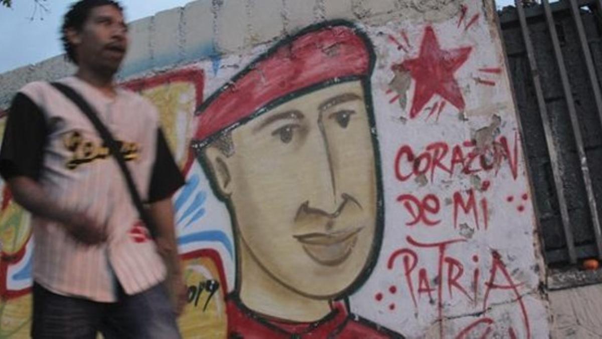 Un hombre camina frente a un muro con la imagen de Chávez pintada.