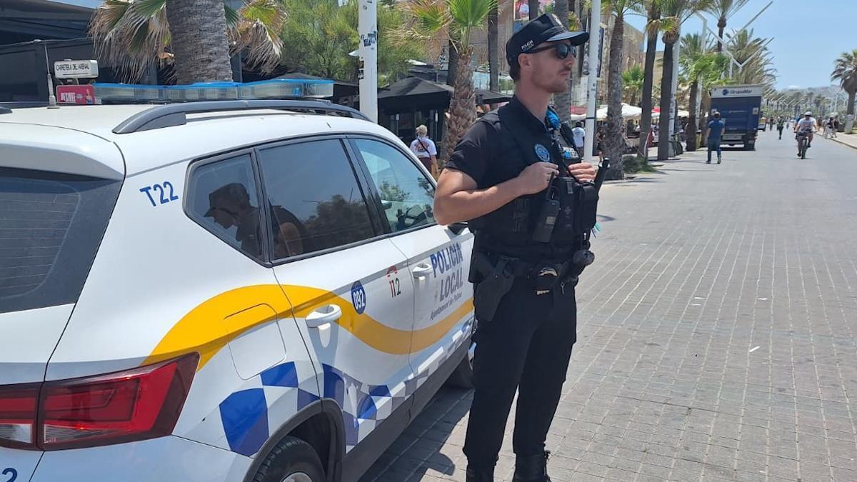 Un agente de la Policía Local de Palma, junto a su coche patrulla, en la Playa de Palma.