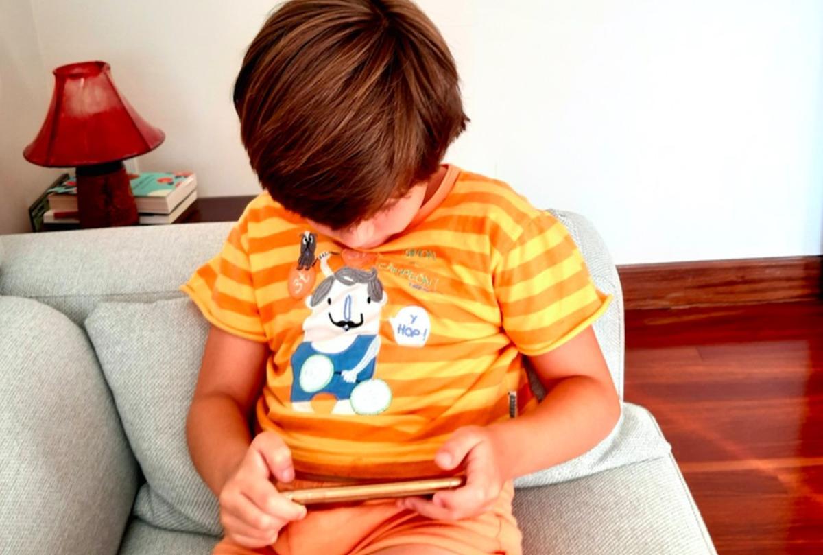 Un niño, en su casa, viendo el móvil.