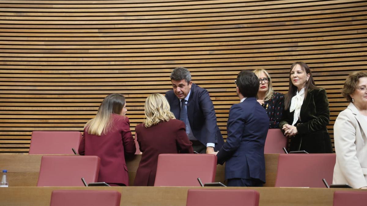 Mazón saluda a sus nuevos compañeros de escaño en la última fila de las Corts.