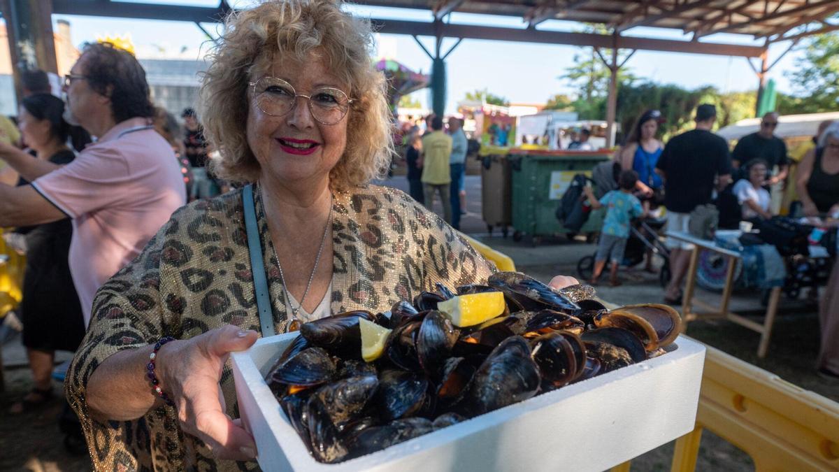 Una mujer sostiene una bandeja de mejillones en una fiesta gastronómica gallega.