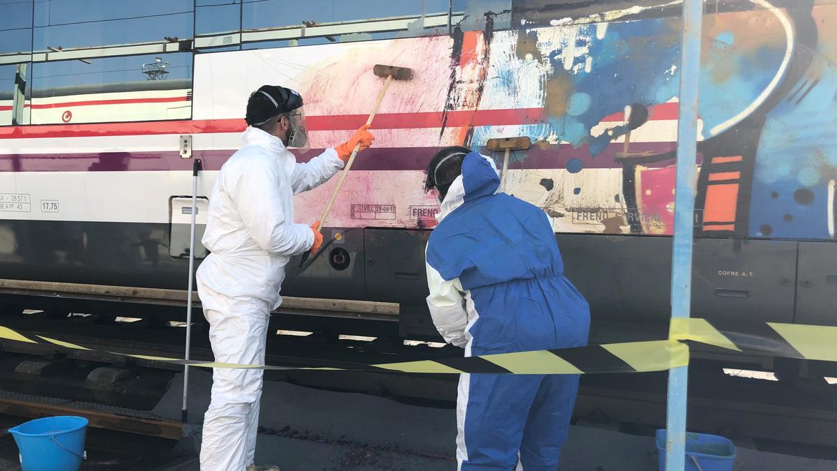 Dos operarios limpian grafitis en un tren de Renfe.