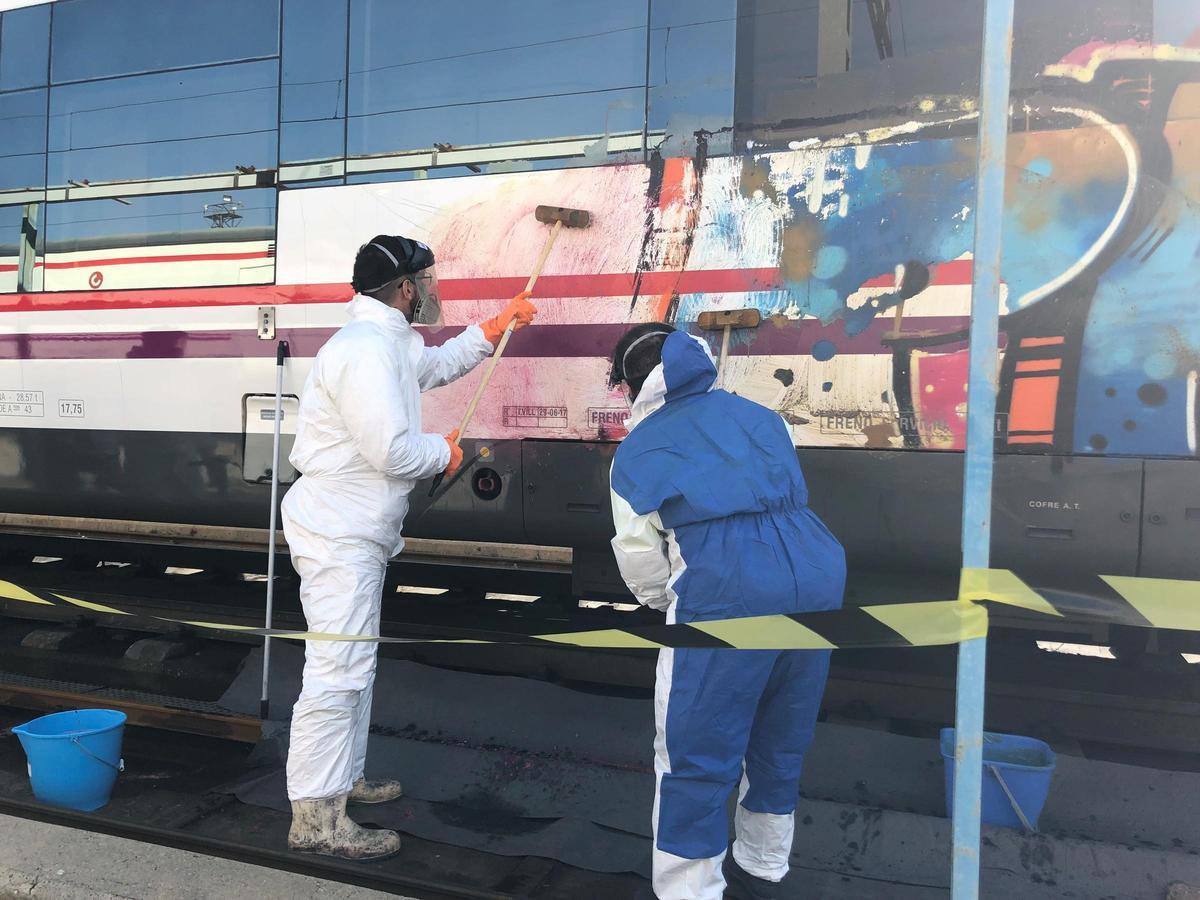 Dos operarios limpian grafitis en un tren de Renfe.