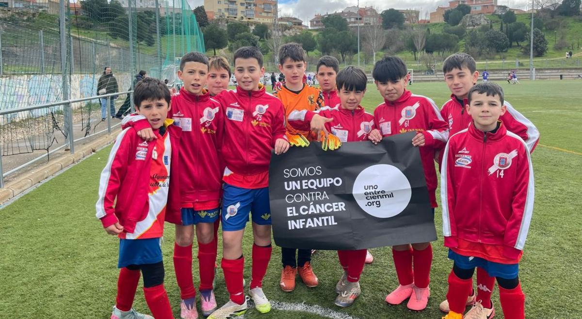 Varios niños del equipo posan con la pancarta de la campaña solidaria.