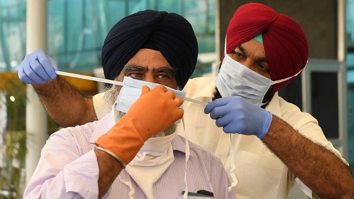 Un parlamentario indio coloca la máscara a un ciudadano en un aeropuerto indio el 8 de mayo del 2020