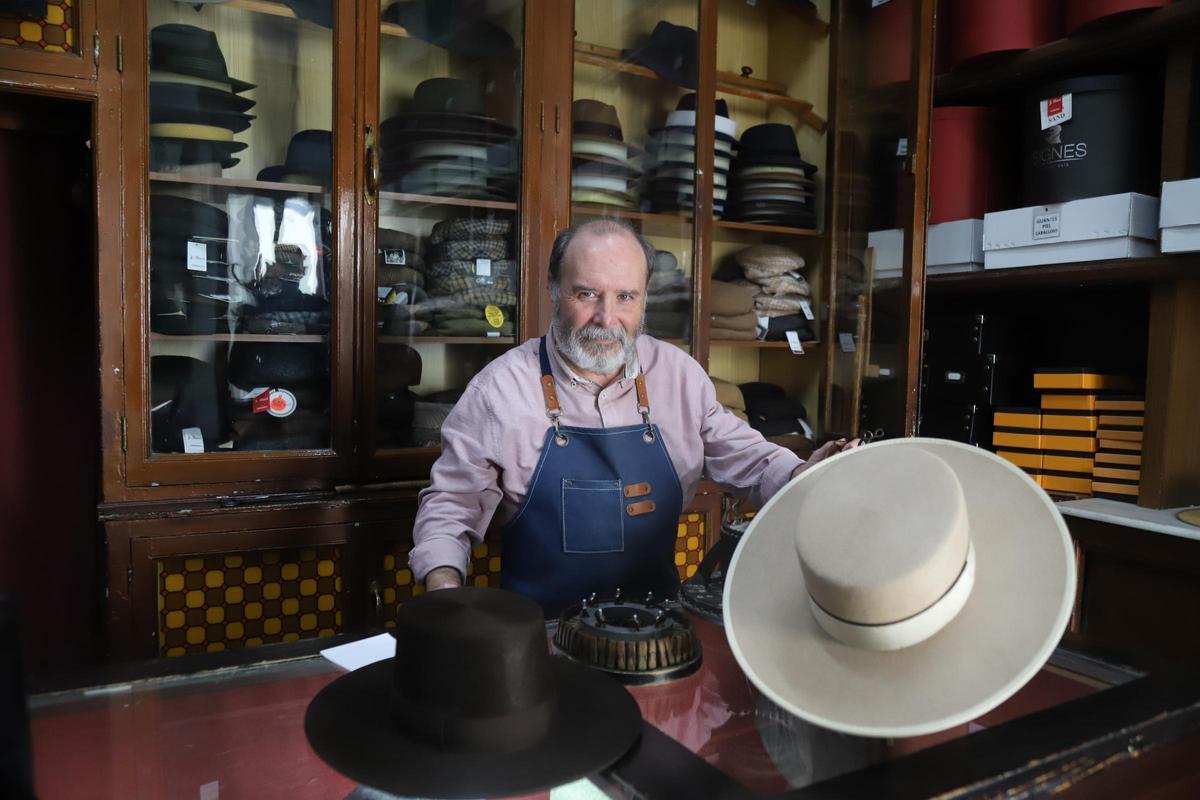 Mario Roldán sostiene dos sombreros cordobeses tras el mostrador de Sombrería Rusi.