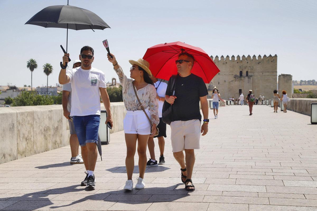 Los turistas de protegen con sombrillas del calor por el Puente Romano de Córdoba.