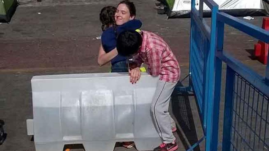 Dos de los niños abrazan a la voluntaria. Detrás, tiendas de campaña instaladas en el puerto.