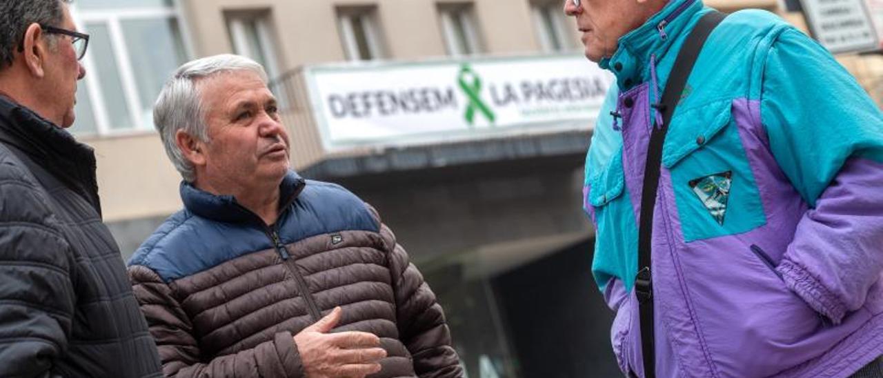 El concejal de Agricultura de Alcarràs, Agustí Camarasa (en el centro) charla con dos vecinos ante la pancarta de apoyo al sector agrario colgada en el ayuntamiento.